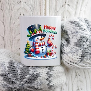 Puede incluir: Taza de cer&aacute;mica blanca con un dise&ntilde;o de mu&ntilde;eco de nieve sonriente, con sombrero de copa negro y bufanda a rayas rojas y blancas, sosteniendo un bast&oacute;n de caramelo y una bola de Navidad. La taza tiene el texto "Happy Holidays".