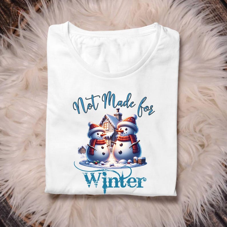 May include: White t-shirt featuring a winter-themed graphic. The design includes two snowmen wearing red hats and scarves, with a house in the background. The text "Not Made for Winter" is displayed above and below the snowmen.