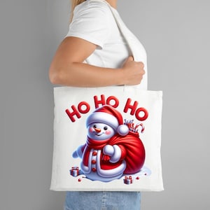 Puede incluir: Bolso de mano blanco con un mu&ntilde;eco de nieve de dibujos animados con bufanda y gorro rojos, y un saco de regalos. Las palabras "HO HO HO" est&aacute;n impresas en rojo. El bolso lo sostiene una persona.