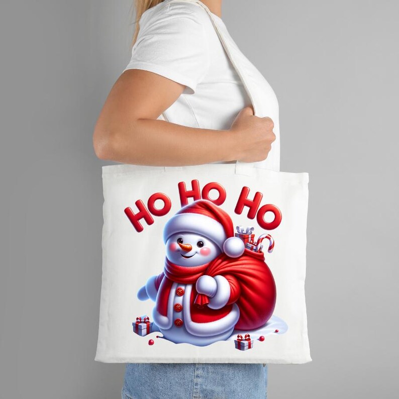 Puede incluir: Bolso de mano blanco con un mu&ntilde;eco de nieve de dibujos animados con bufanda y gorro rojos, y un saco de regalos. Las palabras "HO HO HO" est&aacute;n impresas en rojo. El bolso lo sostiene una persona.