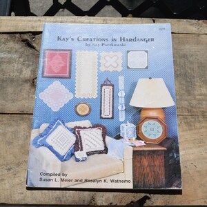 May include: A book titled "Kay's Creations in Hardanger" by Kay Paczkowski. The cover features various Hardanger embroidery examples, including doilies and decorative pieces. The book is compiled by Susan L. Meier and Rosalyn K. Watnemo.