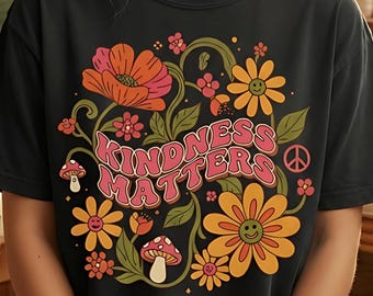 May include: Black t-shirt with a floral design and the text "KINDNESS MATTERS" in pink. The design includes orange and yellow flowers, green leaves, and a peace sign. The shirt is a casual, everyday wear item.