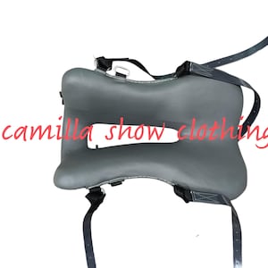 Puede incluir: Un protector de silla de montar gris con correas y herrajes negros. El protector de silla de montar tiene una forma única con un recorte en el centro. El texto "camilla show clothing" está escrito en rosa en la imagen.