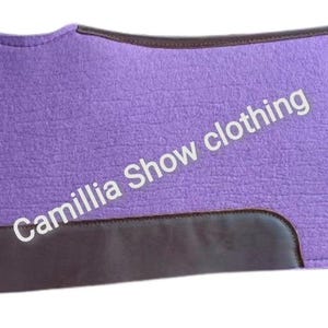 May include: A purple saddle pad with dark brown leather accents. The pad has a textured surface and the text "Camillia Show clothing" is printed on the pad.