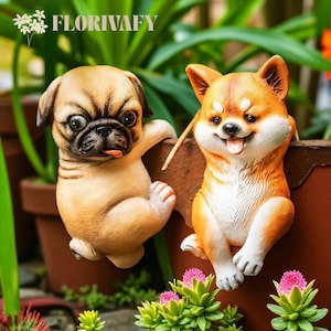 Puede incluir: Dos figuras de perros de cerámica, un pug y un Shiba Inu, están posadas en una maceta marrón. El pug es de color canela con hocico negro, y el Shiba Inu es naranja y blanco. Las figuras están rodeadas de plantas verdes y flores rosas. El texto "FLORIVAFY" está arriba.