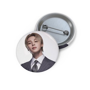 Peut inclure: Deux badges ronds. L'un présente un portrait d'une personne en costume gris, chemise blanche et cravate grise. L'autre montre le dos argenté et l'épingle. Les badges sont à dos argenté.