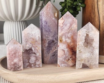 May include: Five polished crystal towers of varying heights, featuring shades of soft pink, lavender, and white with natural druzy inclusions and crystalline textures. The stones are arranged in a row, displaying unique mineral patterns and formations.
