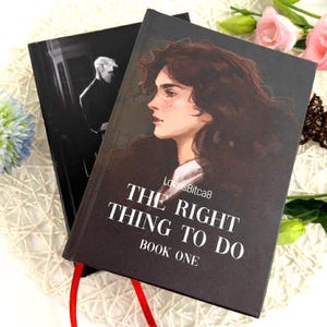 Puede incluir: Dos libros de tapa dura. La portada del primer libro presenta un retrato de mujer y el texto "THE RIGHT THING TO DO BOOK ONE". El segundo libro es negro con una imagen en escala de grises de un hombre. Una cinta roja de marcador es visible.