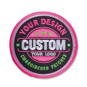 May include: Round embroidered patch with a black background and a pink border. The patch features the text "YOUR DESIGN" and "CUSTOM YOUR LOGO EMBROIDERED PATCHES" in white and green. Three green stars are embroidered above the word "CUSTOM".