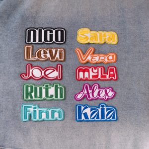 May include: Ten embroidered name patches arranged in two columns on a denim fabric background. The names include Nico in black, Sara in yellow, Levi in brown, Vera in orange, Joel in red, Myla in red, Ruth in green, Alex in purple, Finn in teal, and Kaia in blue.