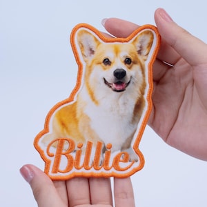 May include: Embroidered patch featuring a smiling corgi dog with orange and white fur. The patch has an orange border and the name "Billie" embroidered in orange script.