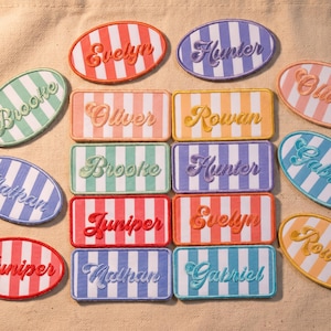 May include: A collection of oval and rectangular embroidered patches featuring vertical stripes in various colors. Each patch displays a name in cursive script, including Evelyn, Hunter, Brooke, Oliver, Rowan, Juniper, Nathan, Gabriel, and Olivia.