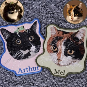 May include: Embroidered patches featuring cat portraits. One patch has a black and white cat with a frog on its head, the name "Arthur" is embroidered below. The other patch has a calico cat, with the name "Mel" embroidered below.