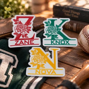 May include: Three embroidered patches featuring large letters Z, K, and N, each decorated with a floral rose pattern. The Z patch is red with the name ZANE, the K patch is green with KNOX, and the N patch is yellow with the name NOVA.