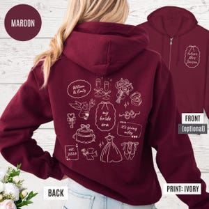 May include: A maroon zip-up hoodie featuring white illustrations and text on the back, including "my bride era" and "it's giving wifey." The front displays "Future Mrs. Jonson." The print is ivory.