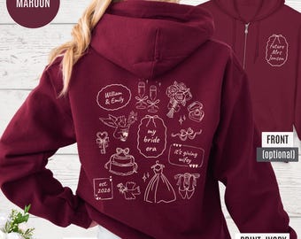 May include: Maroon zip-up hoodie with white graphic illustrations on the back, including text that says "my bride era" and "it's giving wifey." The front of the hoodie has the text "Future Mrs. Jonson." The print color is ivory.