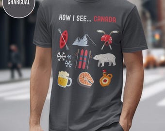 May include: Charcoal gray t-shirt with the text "HOW I SEE... CANADA" and various Canadian icons. The design includes a red canoe, mountains, hockey sticks, snowflakes, skis, a polar bear, beer, salmon, and maple syrup.