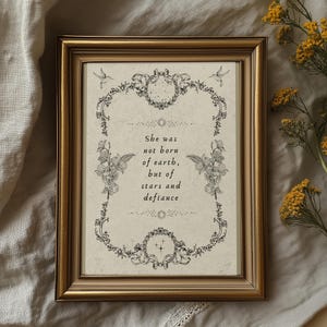 Könnte beinhalten: Ein gerahmter Druck mit einem goldfarbenen Rahmen. Der Druck zeigt den Text "She was not born of earth, but of stars and defiance", umgeben von floralen und Kolibri-Illustrationen in Schwarzweiß.