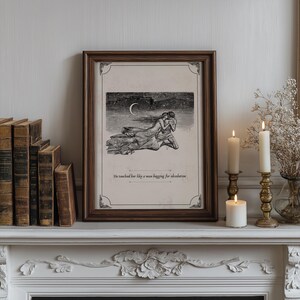 May include: A framed print with a dark wood frame, featuring a black and white illustration of two figures embracing under a crescent moon. The text at the bottom reads, "He touched her like a man begging for absolution."