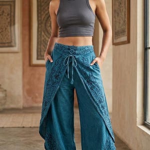May include: A charcoal grey ribbed tank top paired with teal blue wide-leg trousers featuring a wrap-style front, a lace-up drawstring waist, and dark blue embroidered patterns along the edges. The trousers include side pockets and a cropped hem.