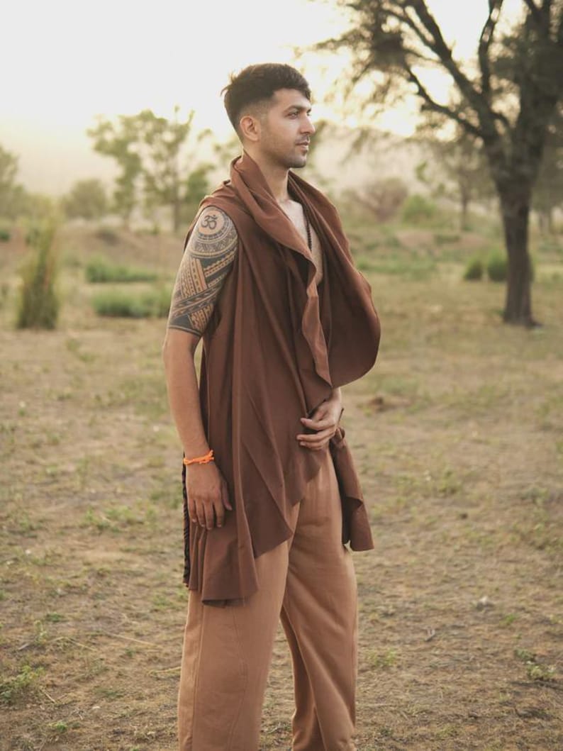 May include: A sleeveless brown wrap vest with an asymmetrical draped front and a wide collar, paired with loose-fitting tan trousers. The vest features a flowing, open-front design that hangs below the waist, creating a layered look with the pants.