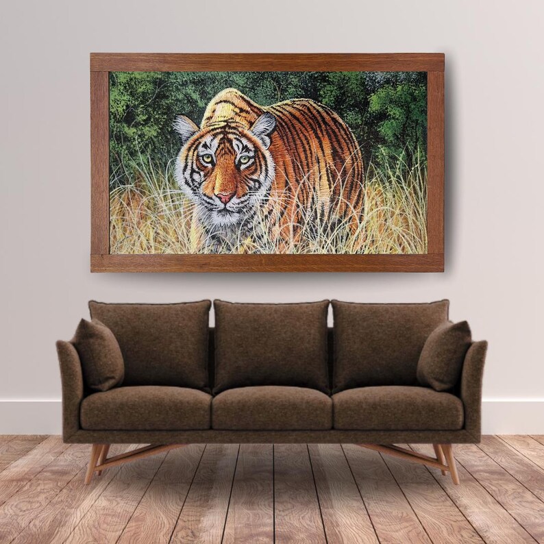May include: A framed artwork featuring a detailed painting of a tiger. The tiger, with orange and black stripes, is set against a backdrop of green foliage and tall grass. The artwork is encased in a dark brown wooden frame, adding a classic touch.