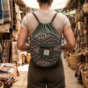 Könnte beinhalten: Ein grüner Rucksack mit Kordelzug und einem kreisförmigen Vorderteil mit schwarz-weißem geometrischem Muster. Eine kleine quadratische Reißverschlusstasche ist vorne mittig angebracht und zeigt ein weißes Etikett mit grünem Blatt-Symbol und dem Text HIMALAYAN.