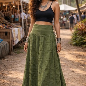 May include: A floor-length olive green skirt featuring a textured, grid-like pattern with frayed edges, a high waistband, and side lace-up detailing. The skirt is paired with a simple black spaghetti strap crop top and silver jewellery accessories.
