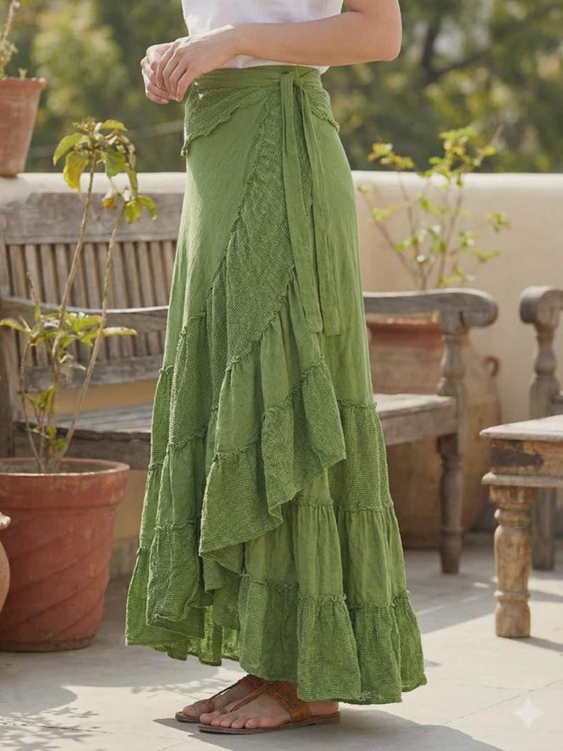 May include: A long, flowing green wrap skirt with a tiered, ruffled design. The skirt features a textured panel on the front and a tie closure at the waist. The skirt is made of a lightweight fabric and is suitable for warm weather.
