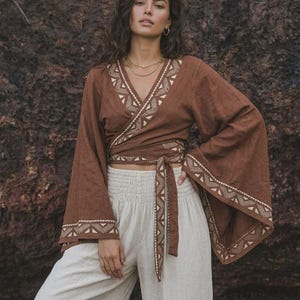 Peut inclure: Un haut portefeuille marron doté de larges manches évasées et d'un décolleté en V, agrémenté d'un motif géométrique crème sur les bords et la ceinture. Le vêtement est associé à un pantalon taille haute clair avec une taille élastique.