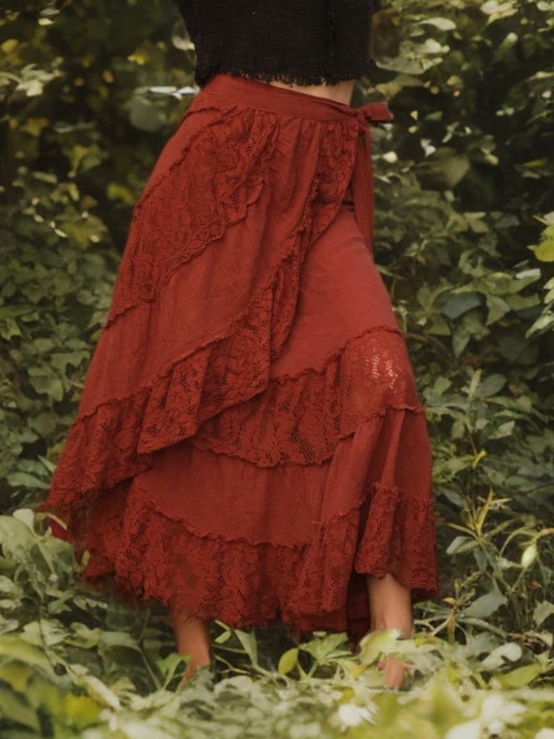May include: A rust-colored, tiered skirt with lace trim. The skirt has a wrap design with a tie closure at the waist. The skirt is made of a soft fabric and has a flowing silhouette. The skirt is suitable for casual wear.