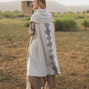 May include: A light gray sleeveless duster vest featuring a draped cowl neckline and a vertical column of black geometric diamond-shaped patterns printed down the center of the back. The garment has an open front and a long, flowing silhouette.