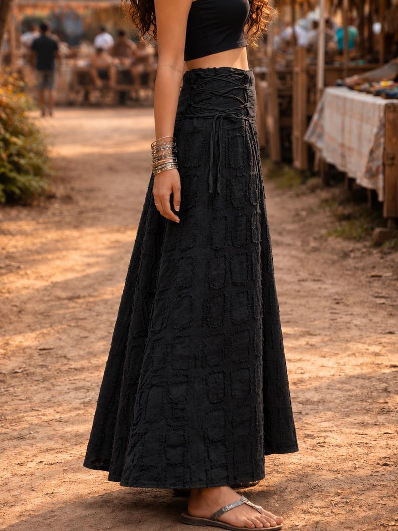 May include: A black maxi skirt featuring a high-waisted design with a lace-up corset-style closure at the waist. The fabric has a textured, repeating rectangular pattern throughout the length of the skirt, which falls to the ankles.