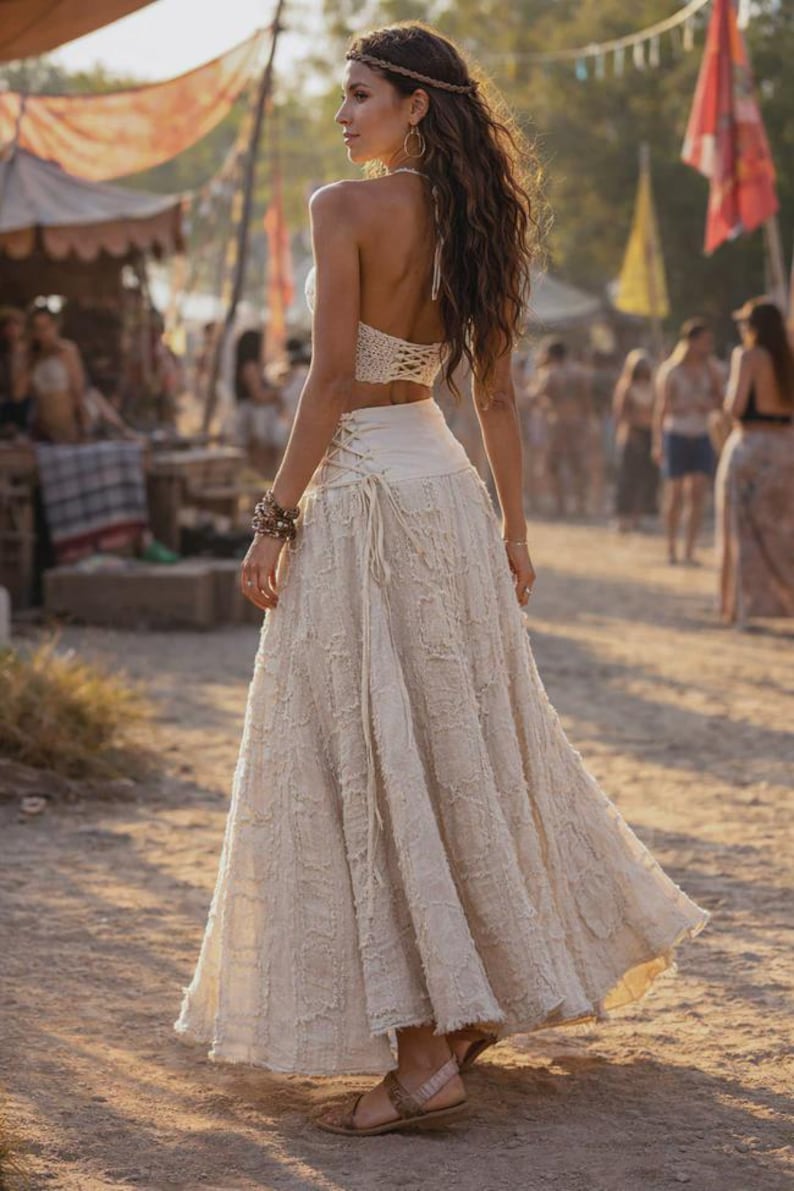 May include: A two-piece outfit consisting of a white crochet halter top and a matching long, textured off-white skirt. The skirt features a high-waisted design with side lace-up detailing and a frayed, layered fabric texture throughout the garment.