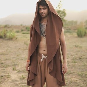 May include: A sleeveless brown hooded vest with an open front and draped fabric panels, paired with light brown drawstring sweatpants. The vest features a large, pointed hood and a flowing, layered design that extends down to the mid-thigh area.