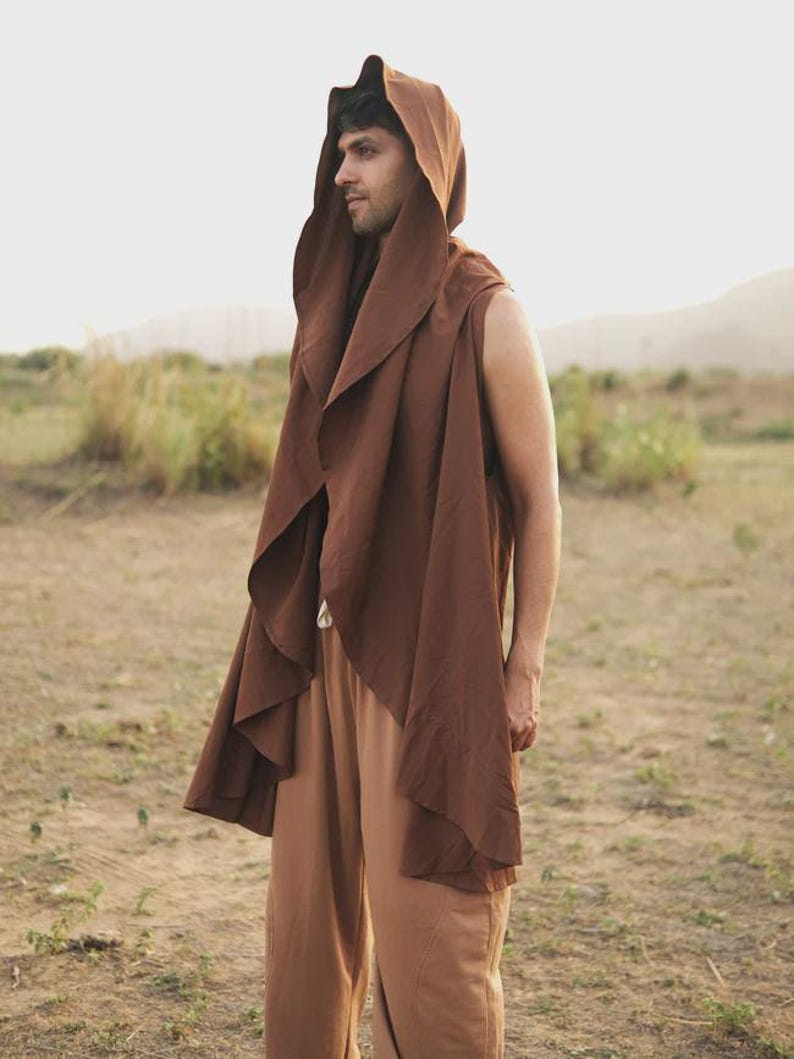 May include: A sleeveless brown hooded vest with an open front and draped fabric panels, paired with light brown trousers. The vest features a large, pointed hood and a long, flowing silhouette that extends past the waistline.