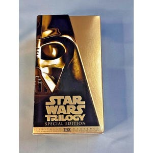 May include: A white ceramic mug with a black handle and the text "But First, Coffee" in a bold, black font. The mug is filled with a dark liquid, likely coffee, and sits on a light-colored surface.