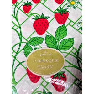 May include: White table cover with a repeating pattern of red strawberries, green leaves, and a green trellis design. The table cover measures 60 inches by 102 inches. The Hallmark label is visible.