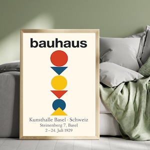 May include: Framed Bauhaus art print featuring a cream background with a red circle, blue triangle, yellow circle, red triangle, and blue triangle. The word "bauhaus" is at the top. Below are details about the Kunsthalle Basel.
