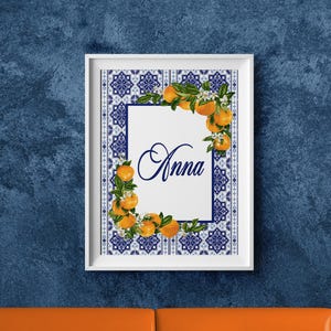 Könnte beinhalten: Ein gerahmter Druck mit dem Namen "Anna" in Schreibschrift. Das Kunstwerk ist von einem blau-weißen Fliesenmuster umgeben und mit Orangen und grünen Blättern verziert. Der Rahmen ist weiß.