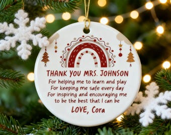 May include: A white ceramic Christmas ornament with a gold string, featuring a rainbow design in red and brown. The ornament has text that reads "THANK YOU MRS. JOHNSON" and a message of appreciation. Decorative Christmas tree and snowflake accents.