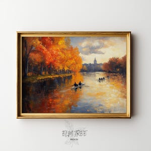 Puede incluir: Pintura al óleo enmarcada que representa una serena escena fluvial con botes de remos. La obra presenta un vibrante follaje otoñal en tonos naranja y amarillo que bordea las orillas del río. El agua refleja los colores de los árboles y el cielo, con un paisaje urbano distante bajo un cielo nublado.
