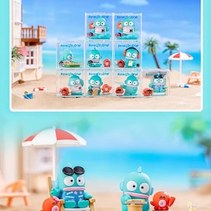 May include: Collection of blue cartoon character figurines in clear display boxes, each with a different accessory. The figurines are displayed on a beach scene with a blue ocean and white sand. Some figurines are in beach chairs.