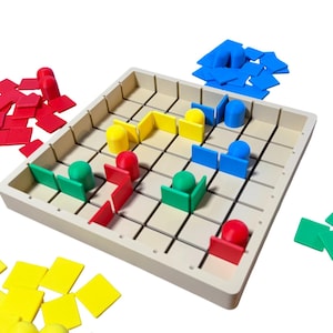 May include: A beige board game with a grid pattern, featuring colourful game pieces in red, yellow, green, and blue. The game pieces include square tiles and cylindrical figures. Scattered around the board are additional game pieces in various colours.