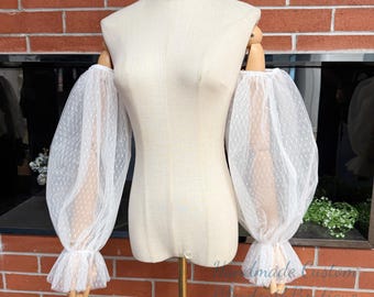 May include: White, sheer, puffy sleeves with a delicate polka dot pattern and ruffled cuffs. The sleeves are displayed on a dress form against a brick wall background. The text "Handmade Custom" and "Elegance with Boutique" is visible.