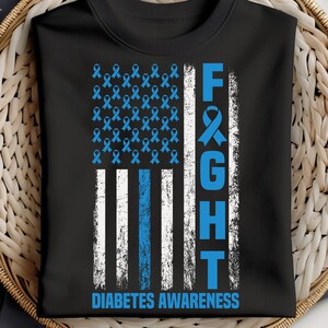 May include: Black t-shirt featuring a distressed American flag design with blue ribbons and stripes. The word "FIGHT" is vertically aligned, and the text "DIABETES AWARENESS" is at the bottom. The shirt is a symbol of support.