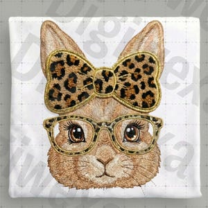 Könnte beinhalten: Gesticktes Design eines Hasengesichts mit goldgerahmter Brille und einer Schleife mit Leopardenmuster. Der Hase hat braunes Fell und detaillierte Gesichtszüge. Das Design befindet sich auf weißem Hintergrund.
