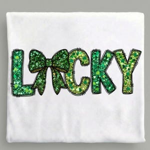 May include: White t-shirt with the word "LUCKY" in green glitter lettering. The letter "O" is replaced with a green bow. The letters are outlined in black. The design is centered on the shirt.