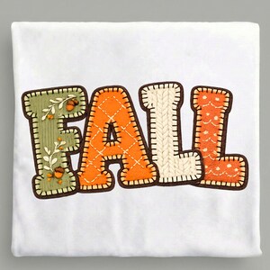 Pode incluir: Uma t-shirt branca com a palavra FALL em letras grandes de estilo bloco. Cada letra tem uma textura distinta: o F é verde sálvia com ilustrações de bolotas, o A é laranja com padrão acolchoado, o L é de malha creme e o L é laranja.