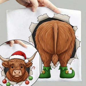 May include: A white t-shirt with a cartoon Highland cow design. The cow's rear end is visible, wearing green elf shoes with bells. A smaller inset shows the cow's face wearing a Santa hat and Christmas decorations.